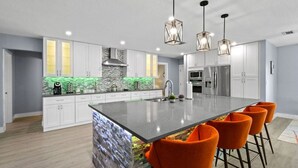 Une cuisine moderne avec des meubles blancs, un îlot central doté de tabourets de bar et un pare-feu vert.