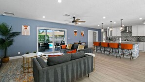 Un salon moderne avec un canapé gris, des fauteuils orange et un coin repas doté d’un bar.