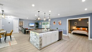 Une cuisine moderne dotée d’un îlot central, un coin repas avec une table et des chaises, et une chambre à coucher avec un lit et une table de chevet.