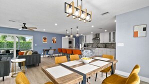 Une cuisine moderne avec des meubles blancs, un pare-feu en pierre et un coin repas comprenant une table en bois et des chaises jaunes.