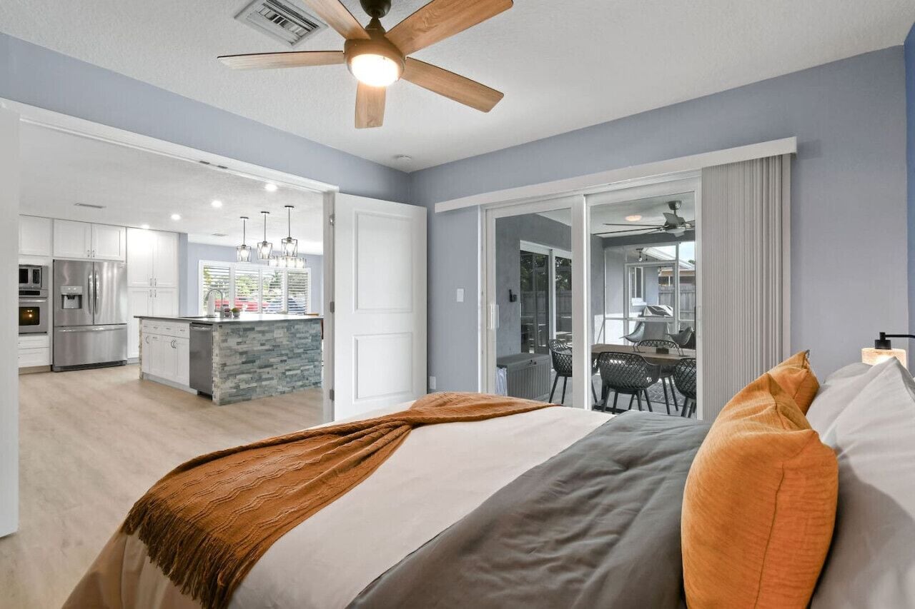 Une chambre d’hôtel moderne dotée d’un grand lit, d’un ventilateur de plafond et offrant une vue sur la cuisine et l’espace repas.