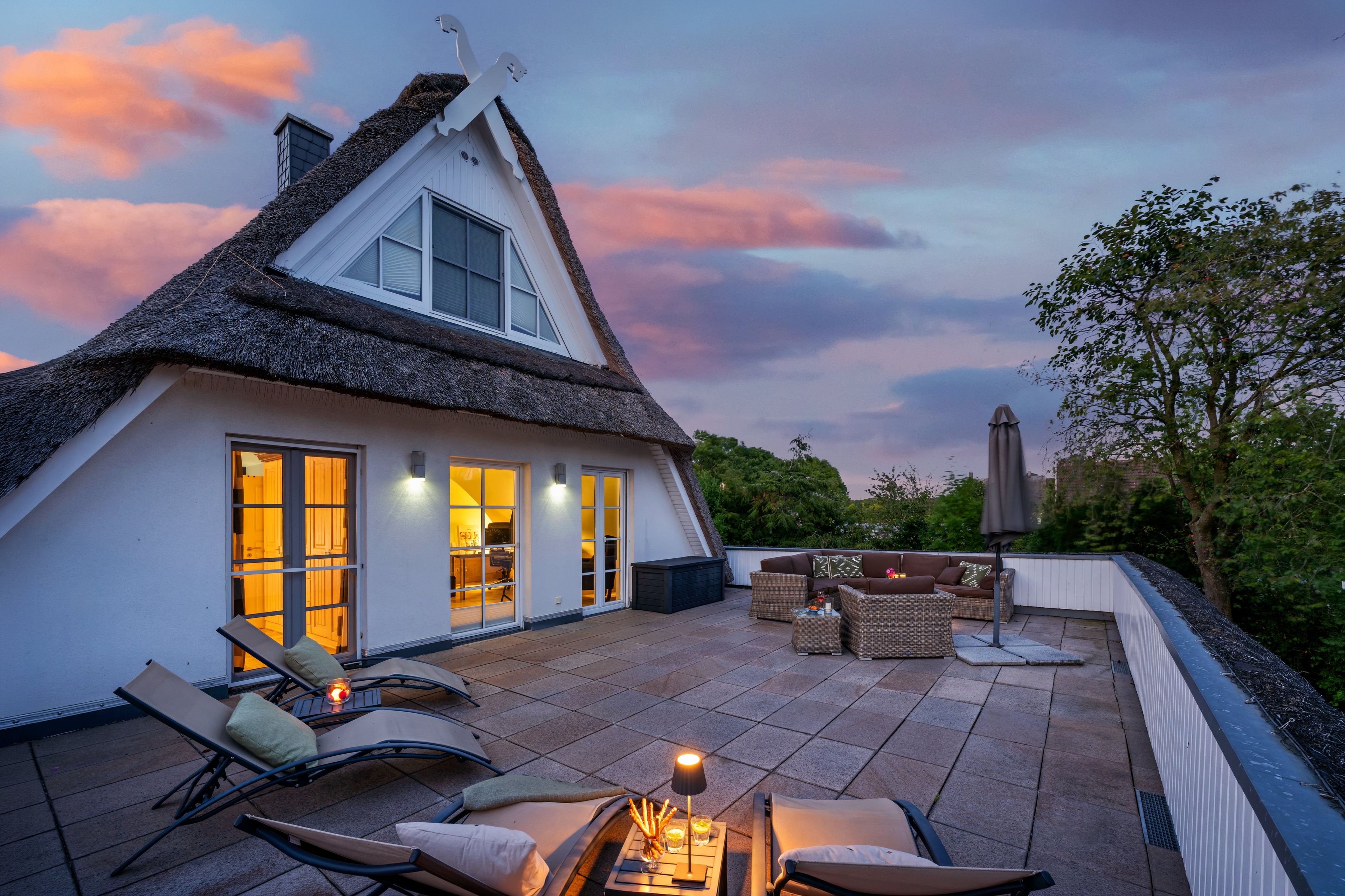 A thatched-roof house with a patio area featuring outdoor furniture and a table with candles.