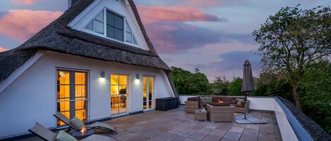 A thatched-roof house with a patio area featuring outdoor furniture and a table with candles.