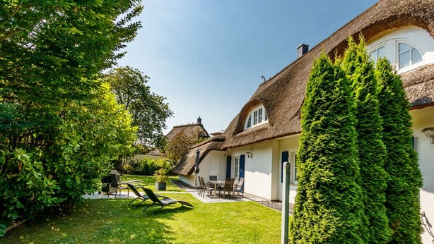 A thatched-roof house with a well-maintained lawn and outdoor seating area.