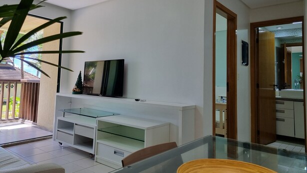 Ein modernes Interieur mit einem Esstisch mit Glasplatte, einer weißen Unterhaltungsanlage und einer großen Topfpflanze.