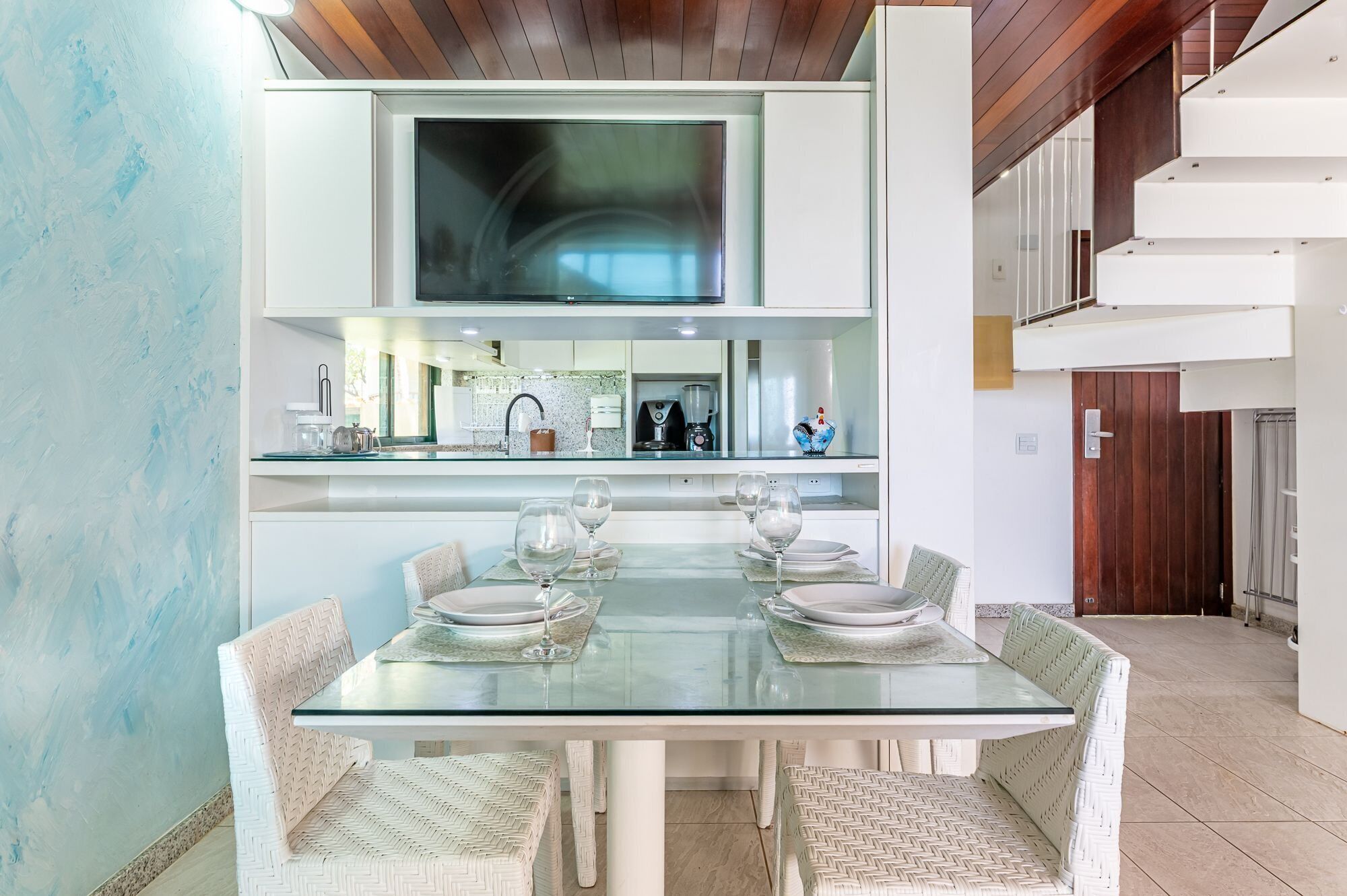 Un comedor moderno con una mesa de vidrio, sillas blancas y una cocina al fondo.