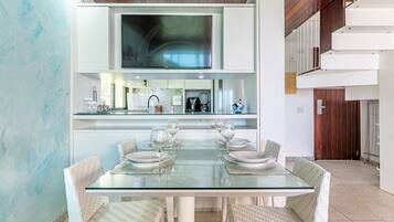 Un comedor moderno con una mesa de vidrio, sillas blancas y una cocina al fondo.