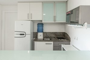 Uma cozinha compacta com geladeira, dispenser de água, micro-ondas e pia.