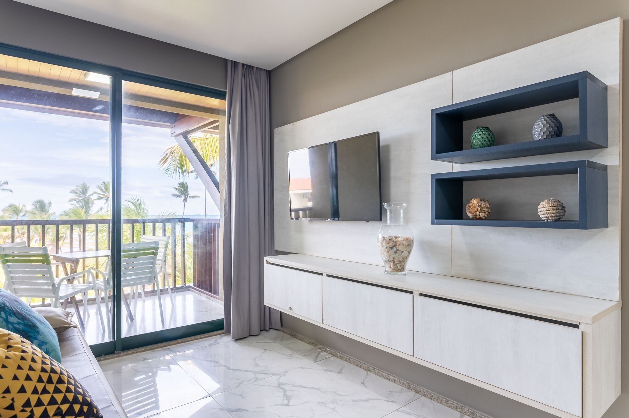 Quarto moderno com varanda, televisão de tela plana e objetos decorativos nas prateleiras.