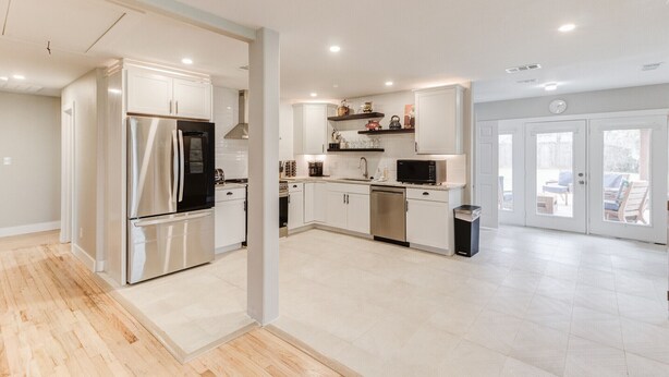 Una cocina moderna con electrodomésticos de acero inoxidable, armarios blancos y piso de baldosas.