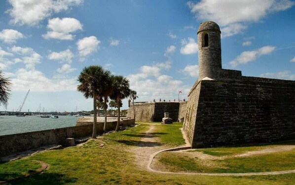 A coastal fort with a stone tower, a grassy pathway, and a view of the sea and boats. - ~Hot Tub~2 King Beds~3 Bedrooms~Walk to Beach, Free Parking, Close to Downtown (St. Augustine)