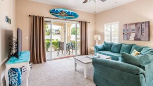 A living room with a teal sofa, a coffee table, a TV, and a ceiling fan. - ~Hot Tub~2 King Beds~3 Bedrooms~Walk to Beach, Free Parking, Close to Downtown (St. Augustine)