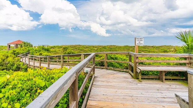 A wooden boardwalk leading through a lush green landscape with a 'DO NOT LITTER IN DUNES' sign. - ~Hot Tub~2 King Beds~3 Bedrooms~Walk to Beach, Free Parking, Close to Downtown (St. Augustine)