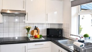 A modern kitchen with white cabinets, a black countertop, a microwave, and a window with a view. - Lodge 3 - Lytton Tree Lodge (Reydon)