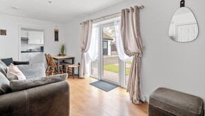 A modern living room with a sofa, a dining table, and a kitchen in the background. - Lodge 3 - Lytton Tree Lodge (Reydon)