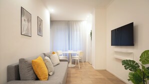A modern living room with a grey sofa, a dining table with chairs, a flat-screen TV mounted on the wall, and a potted plant. - IV HOUSE 
Luxurious apartment in Rome (Roma)