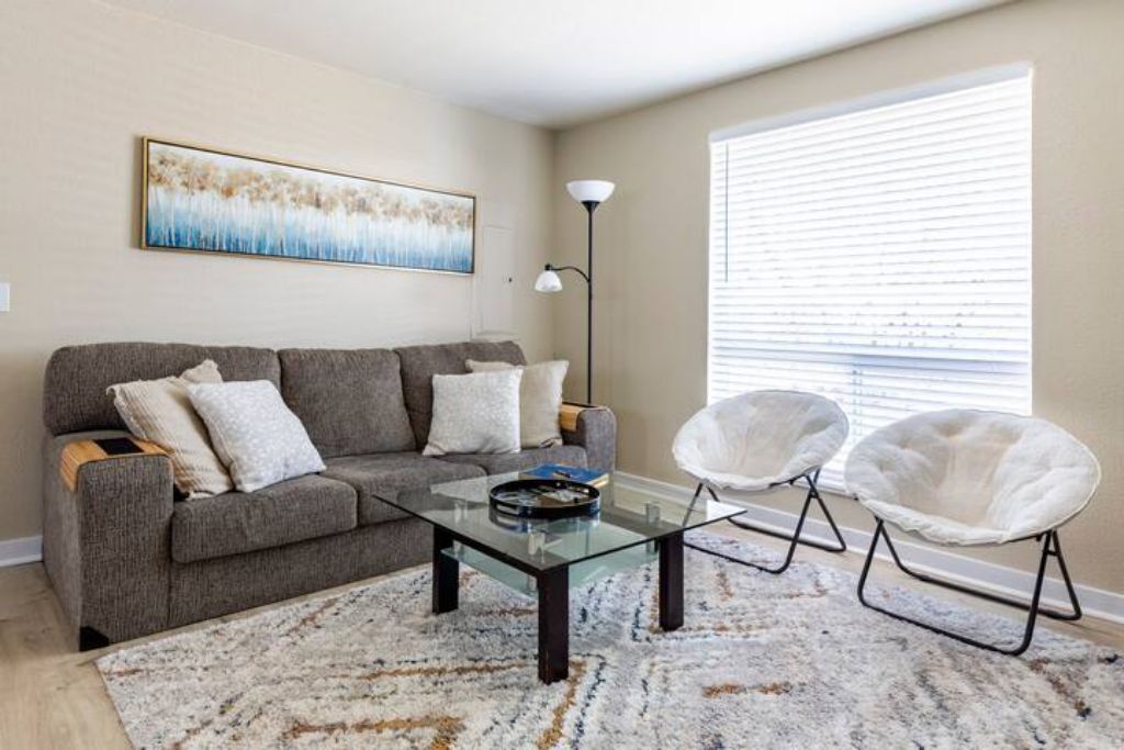 A living room with a grey sofa, a glass coffee table, and two white armchairs.