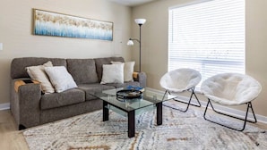 A living room with a grey sofa, a glass coffee table, and two white armchairs. - The Sunshine House (Sequim)