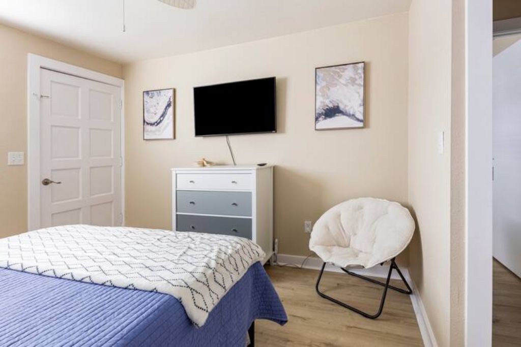 Une chambre à coucher avec un lit, une commode, une chaise et un téléviseur fixé au mur.