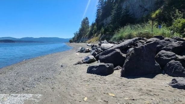 A rocky shoreline with a clear view of the water and distant mountains. - The Sunshine House (Sequim)