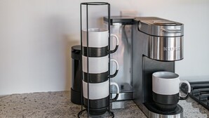 Una cucina con una macchina da caffè, una caraffa di vetro e una tazza sul bancone.