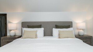 Un letto rifatto con due cuscini, una testiera grigia e due lampade sui comodini in legno.