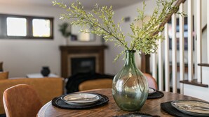 Un tavolo da pranzo con un vaso verde, piatti e una sedia in una stanza con una scala e un camino.