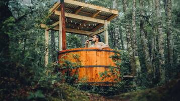 A rustic wooden hot tub in a forest setting.