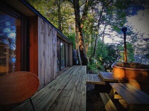 A wooden deck with a glass wall, a woven chair, and a hot tub.