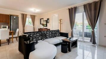 A modern living room with a sofa, a dining table, and a kitchen area.