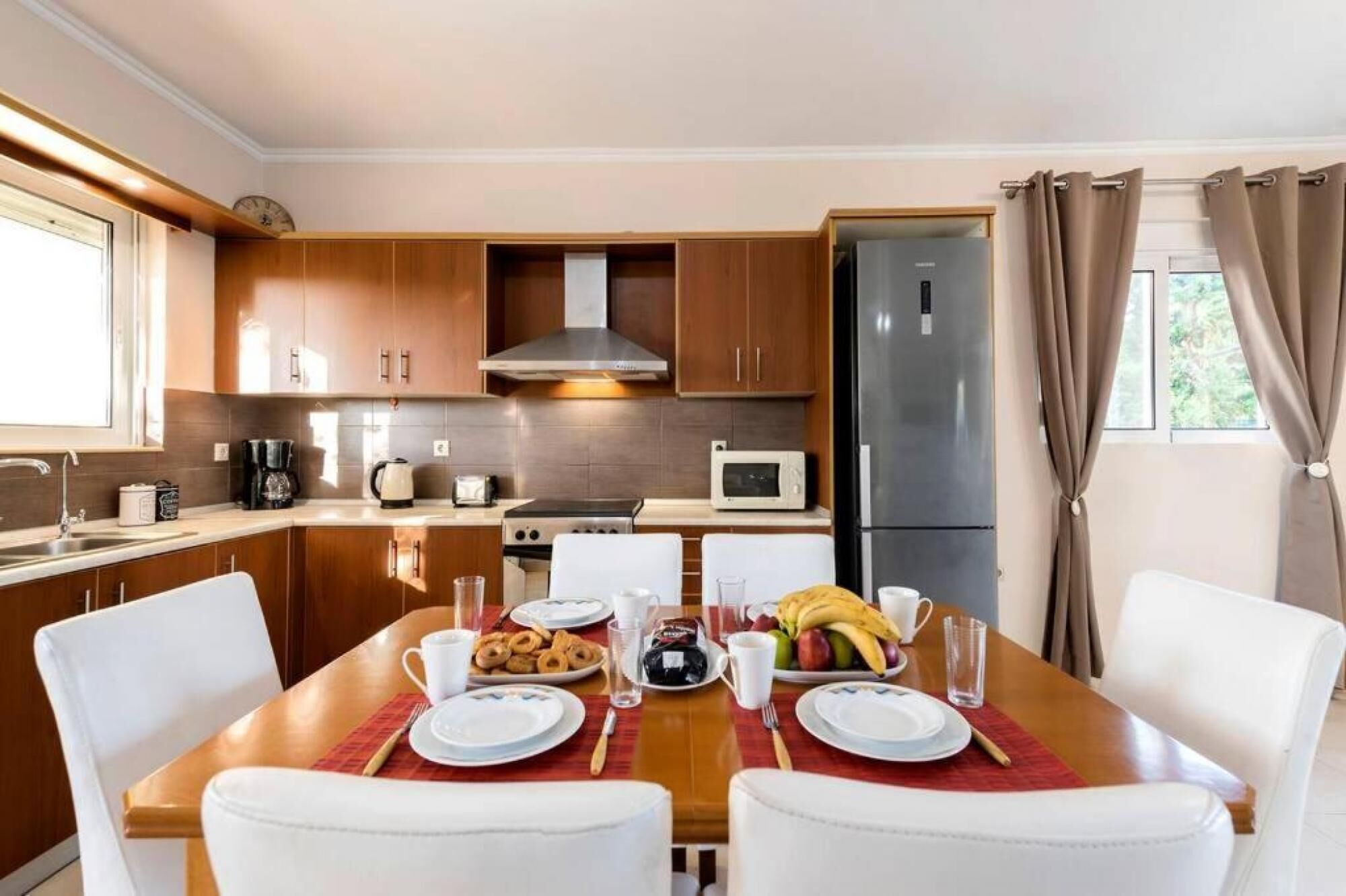 Una cocina moderna con armarios de madera, un refrigerador de acero inoxidable y una mesa de comedor preparada para el desayuno.