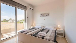 A bedroom with a large bed, two bedside tables with lamps, a wall-mounted air conditioner, and a view of the outdoors through a sliding glass door. - Angels Villa in Kremasti Near the Beach (Rhodes)