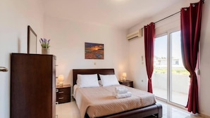 A hotel room with a bed, a dresser, a painting on the wall, and a view through the window. - Angels Villa in Kremasti Near the Beach (Rhodes)