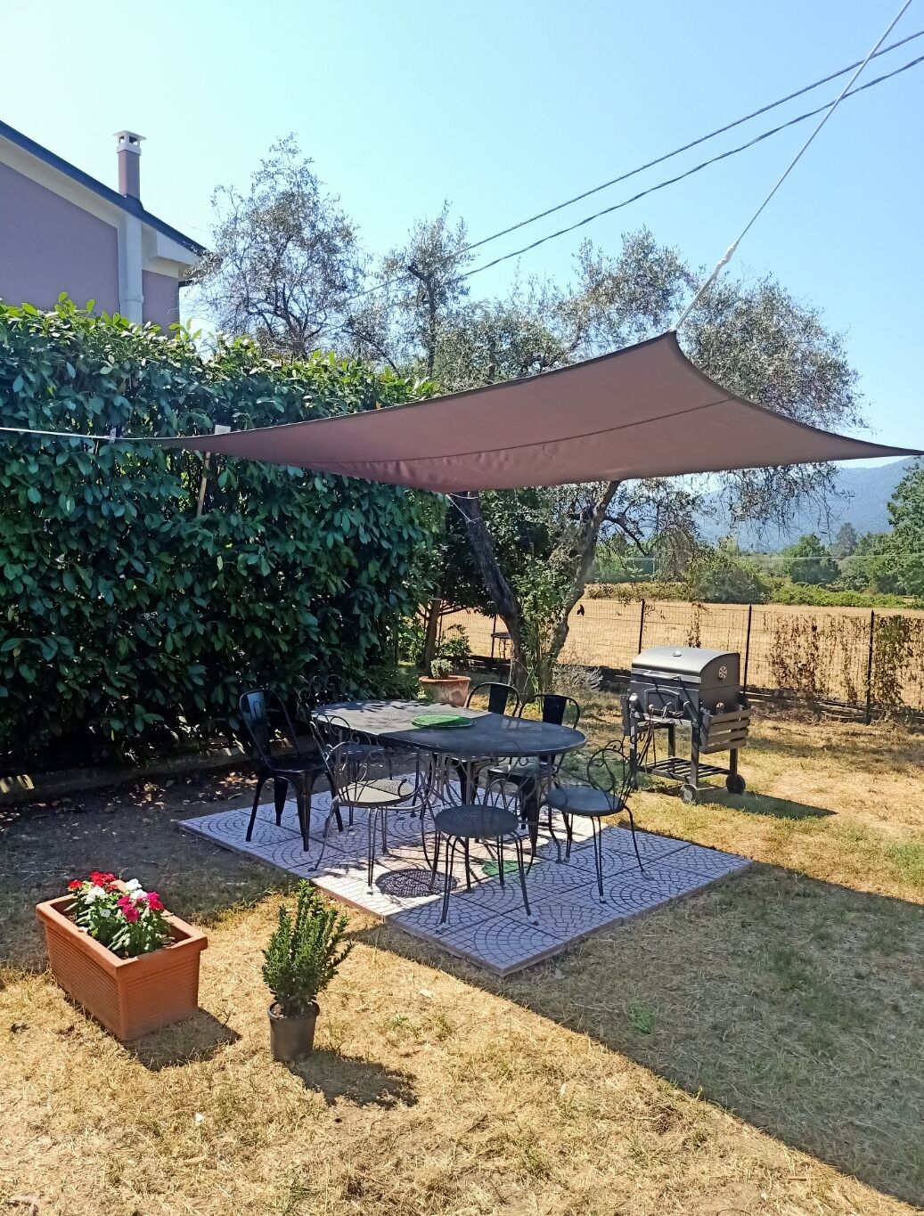 Un espace patio aménagé avec une table et des chaises, un barbecue et une grande voile d’ombrage.