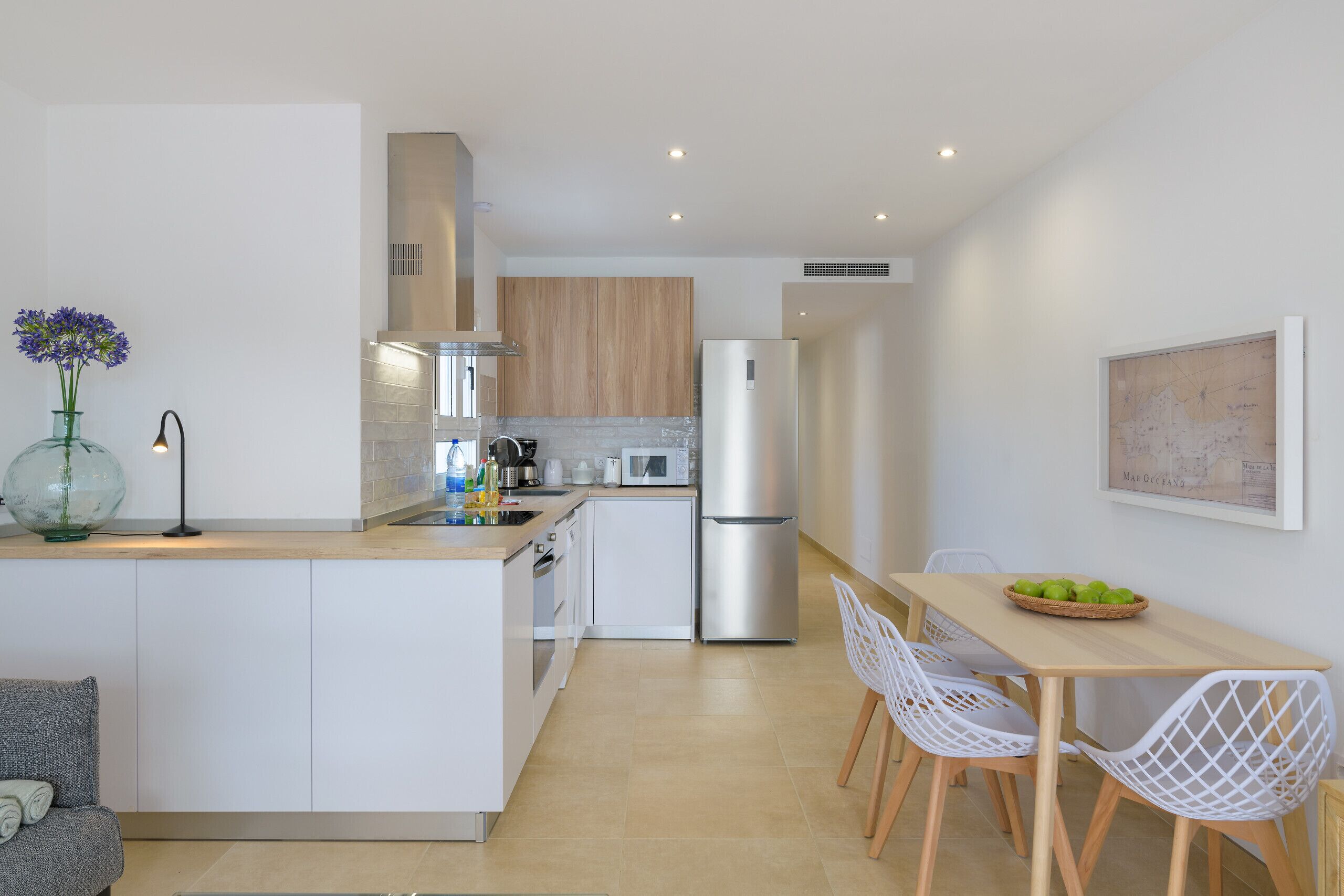 A modern kitchen with white cabinetry, a stainless steel refrigerator, and a wooden dining table with white chairs.