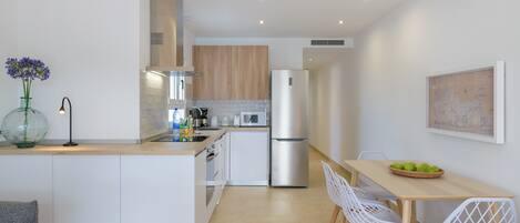 A modern kitchen with white cabinetry, a stainless steel refrigerator, and a wooden dining table with white chairs.