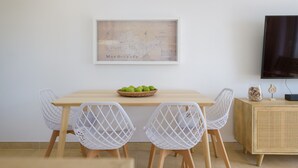 A dining area with a wooden table, white wire chairs, a basket of green apples, a framed map on the wall, and a television on a wooden cabinet. - Casa Anzuelo, with Balcony Puerto del Carmen (Puerto del Carmen)