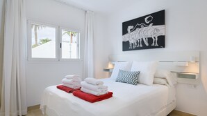 A neatly made bed with white and red towels, a wall-mounted artwork, and a window with curtains. - Casa Anzuelo, with Balcony Puerto del Carmen (Puerto del Carmen)