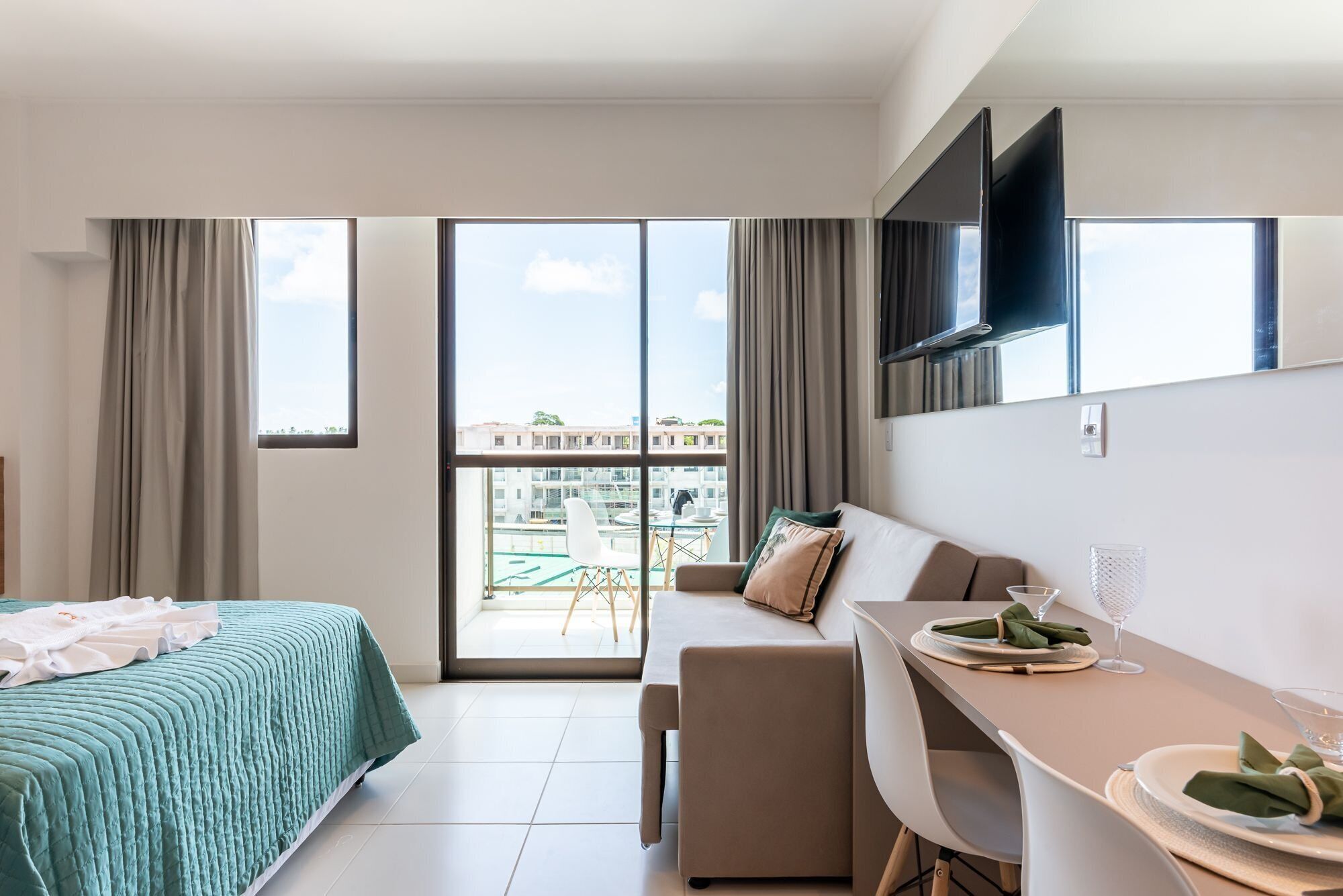 Una habitación de hotel moderna con cama, sofá, mesa de comedor y vista panorámica de la ciudad a través de amplias ventanas.