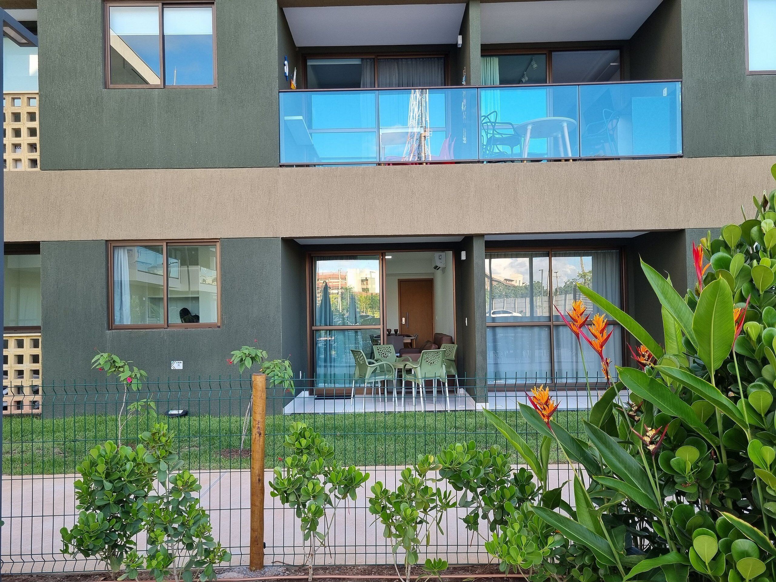 A two-story building with a balcony, a fenced garden area, and a visible entrance with a door.