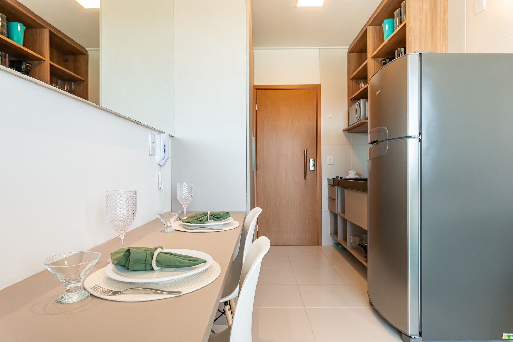 A modern kitchen with a dining table set for two, a refrigerator, and wooden cabinets.
