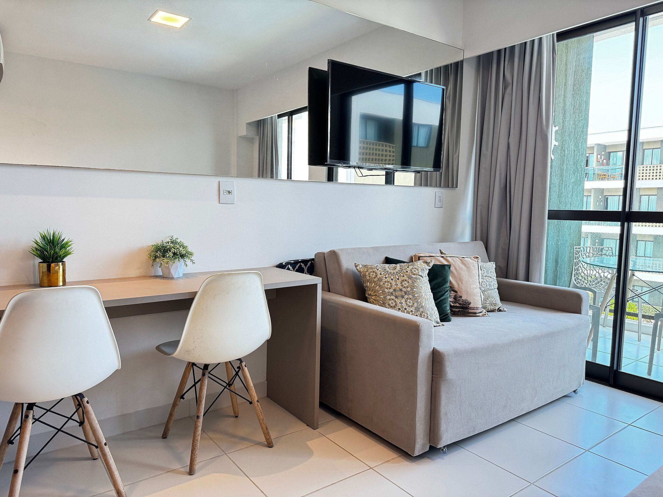 Een moderne woonkamer met een bank, twee fauteuils, een flatscreen-tv en een raam met gordijnen.