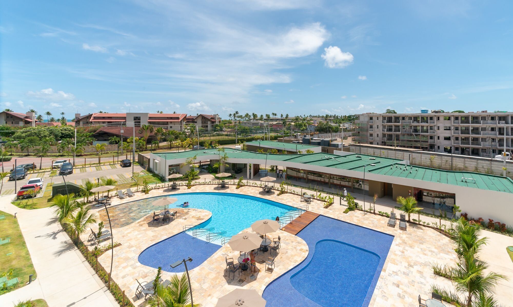 A resort with a large swimming pool, outdoor seating, and a view of surrounding buildings.