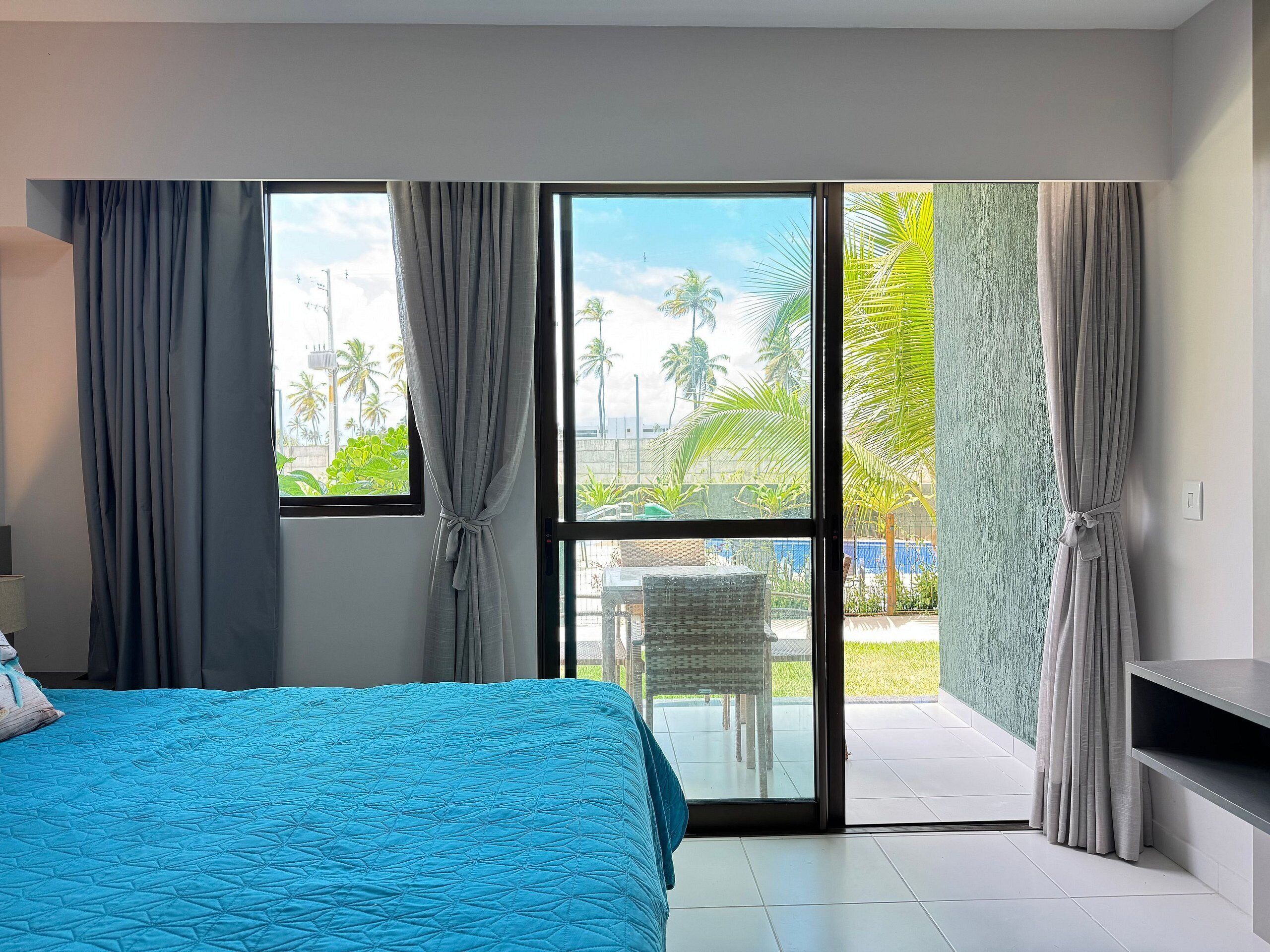 Un dormitorio con cama, cortinas, vistas a palmeras y un balcón.