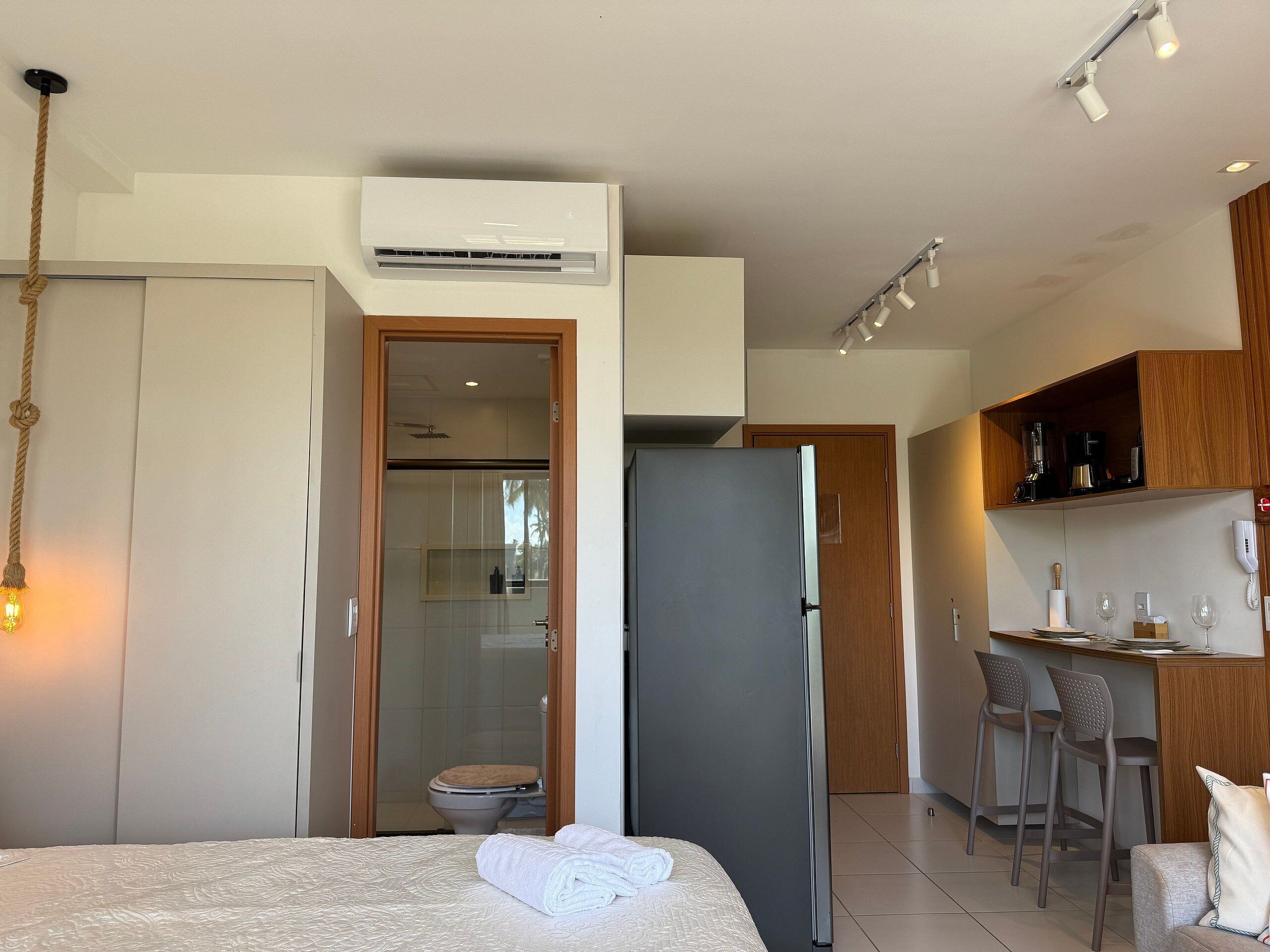 A modern hotel room with a bed, a bathroom, a kitchenette, and a seating area.