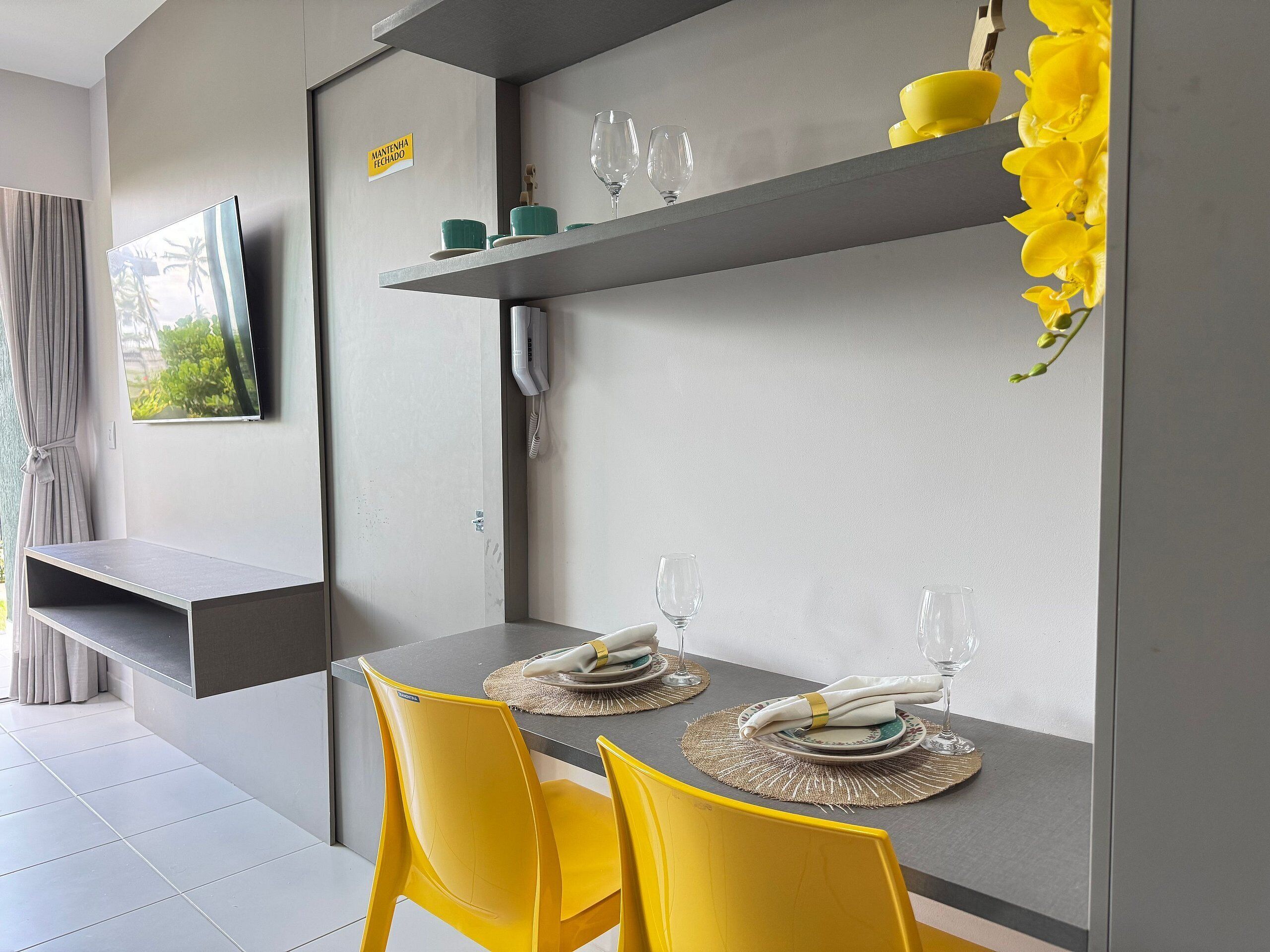 Un comedor moderno con una mesa gris, sillas amarillas y un televisor de pantalla plana montado.