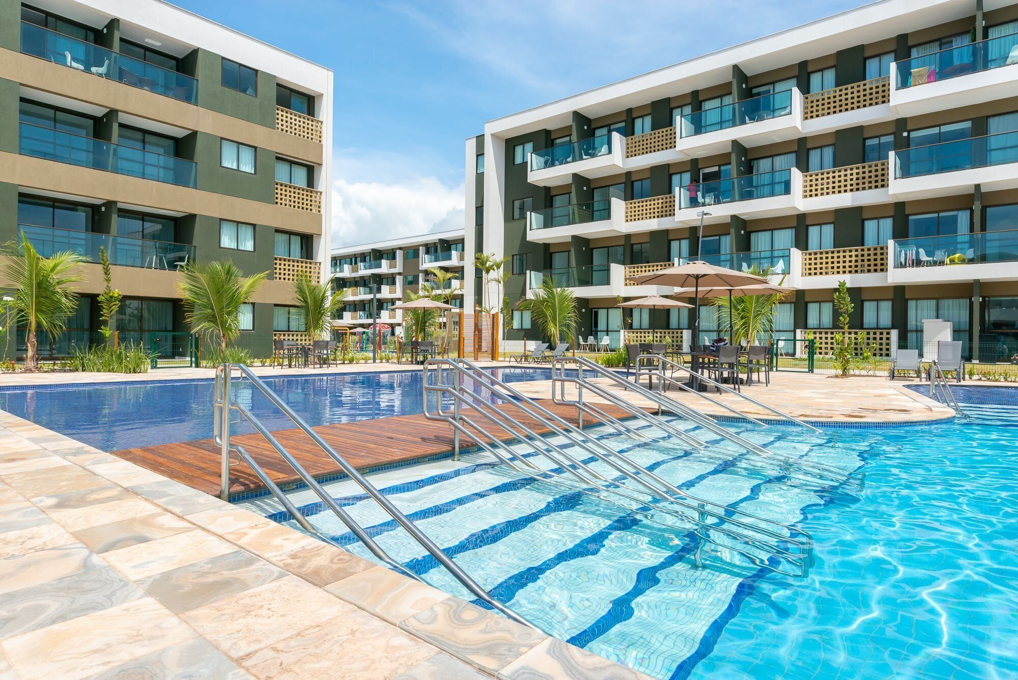 Un hotel moderno con piscina, varios balcones y zonas de estar al aire libre.