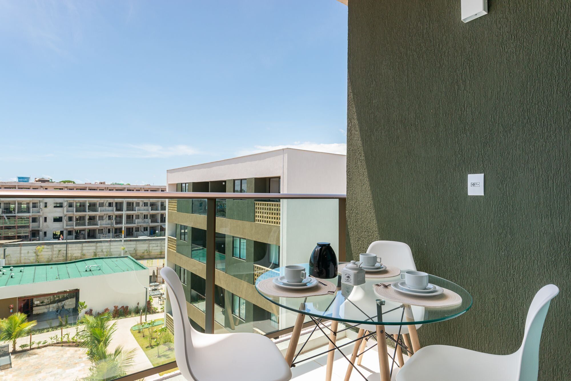 A balcony with a glass table and chairs, overlooking a courtyard with buildings and a green-roofed structure.