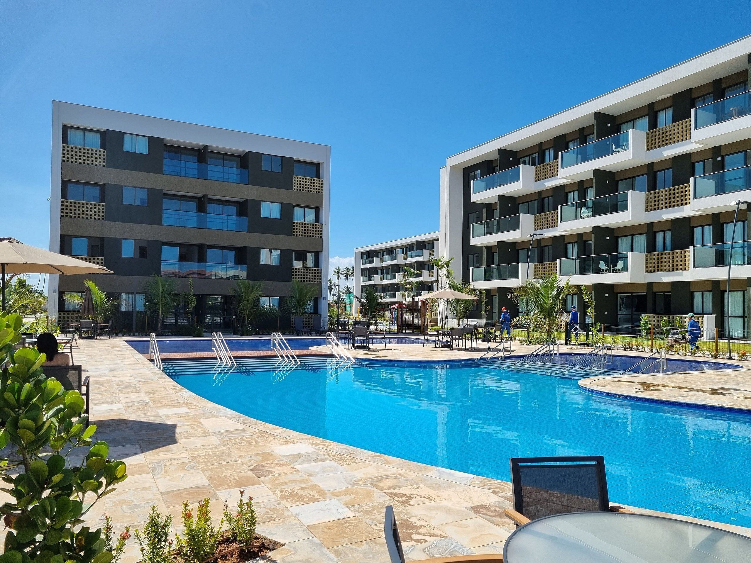 Een modern hotel met een zwembad, terras en helderblauwe lucht.