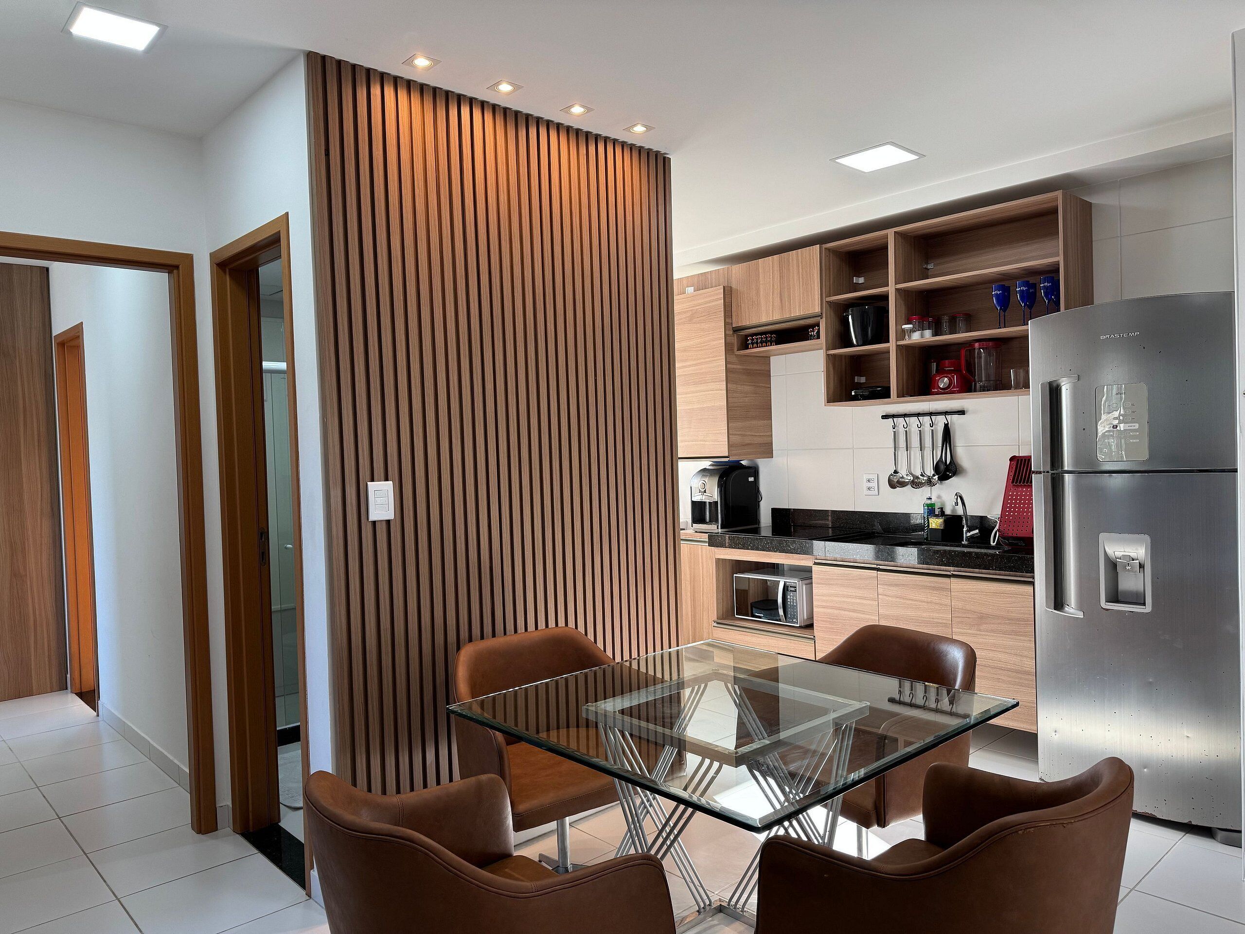 A modern kitchen with a glass-top table and brown chairs, a stainless steel refrigerator, and wooden cabinetry.
